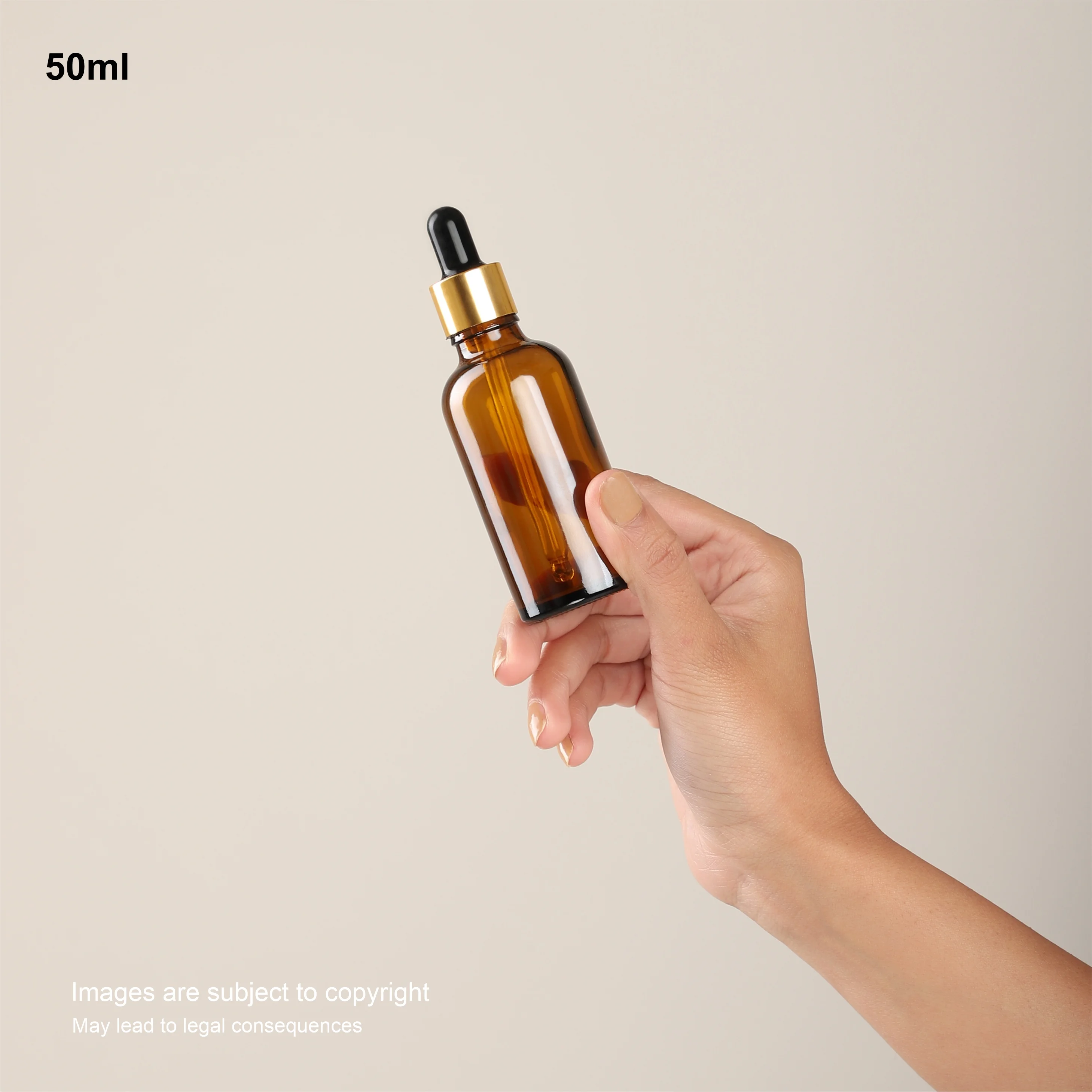 Hand holding 50ml amber glass dropper bottle, gold collar and black bulb, 18/410 neck.